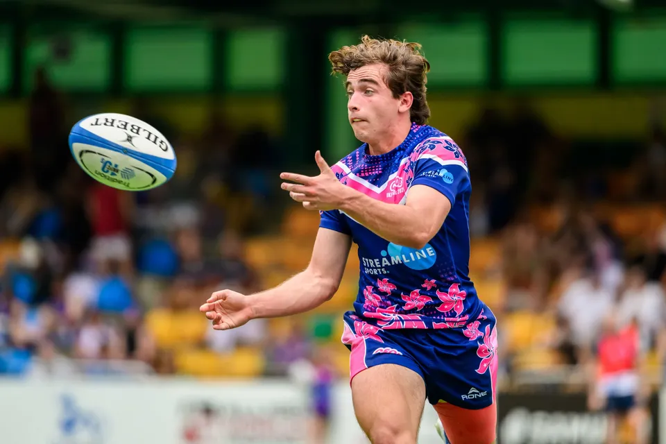 OSOB player in pink and blue releases a pass, the ball in the air beside him, with a blurred crowd behind