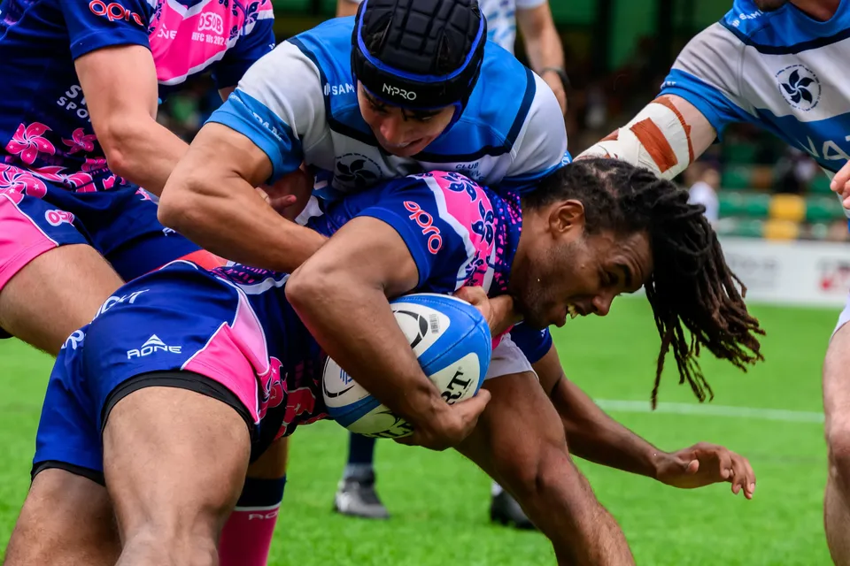 Tight crop of an OSOB ball carrier clutching the ball while an HKFC Natixis player in a scrum cap grabs him