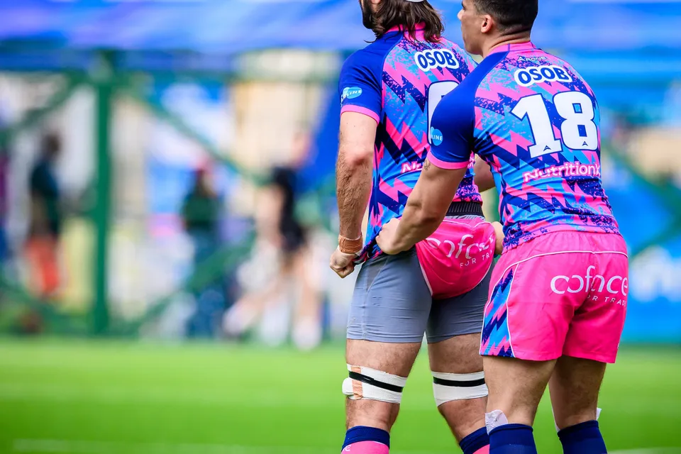 Two OSOB players seen from behind on the pitch, one wearing number 18, with white strapping on their legs