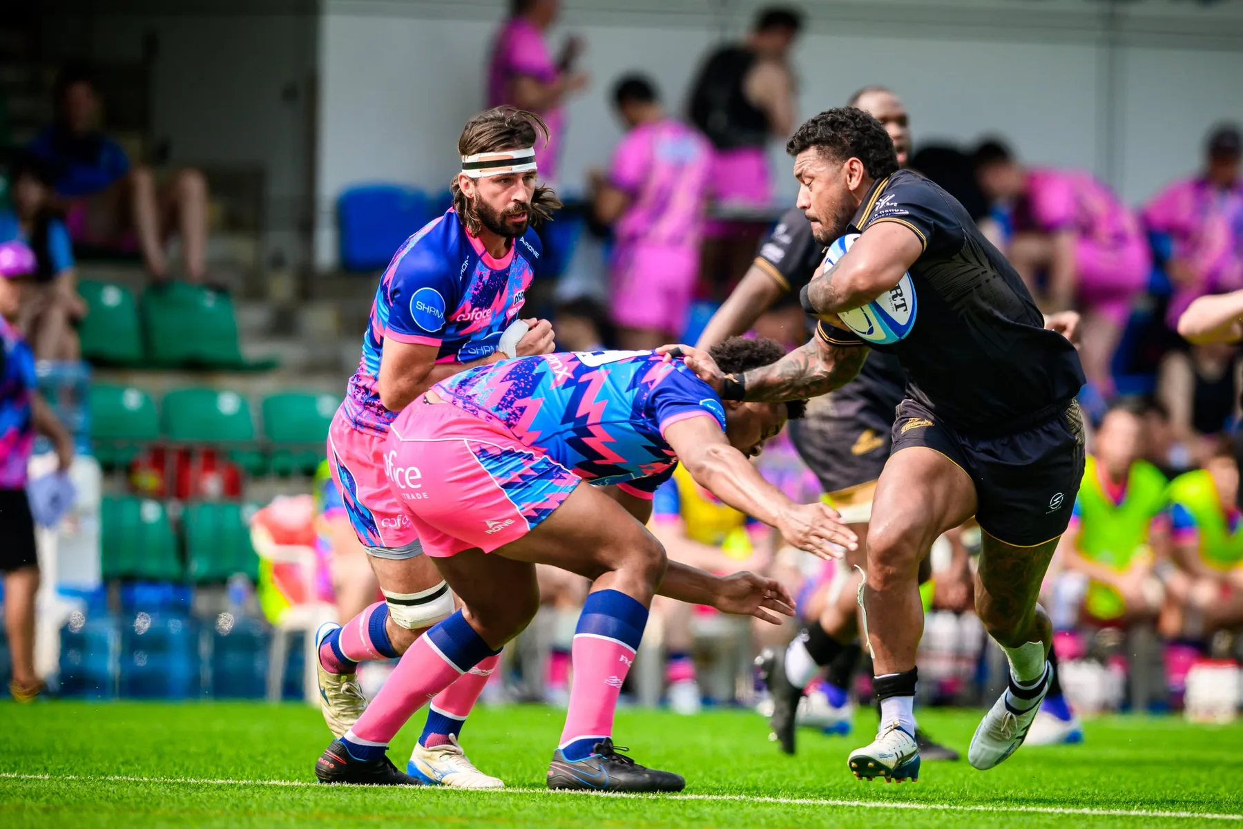 Tropics ball carrier in black drives into a low OSOB tackle as a bearded teammate in pink and blue closes in
