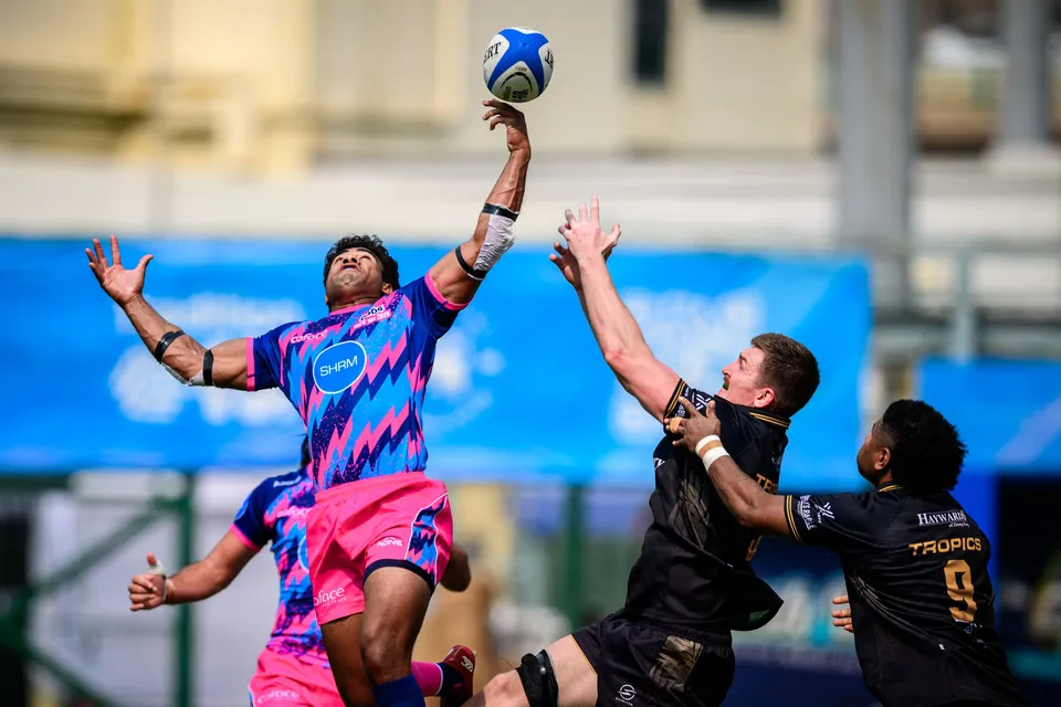 OSOB jumper stretches high to catch a line-out ball as two Tropics players in black reach beneath a blue banner