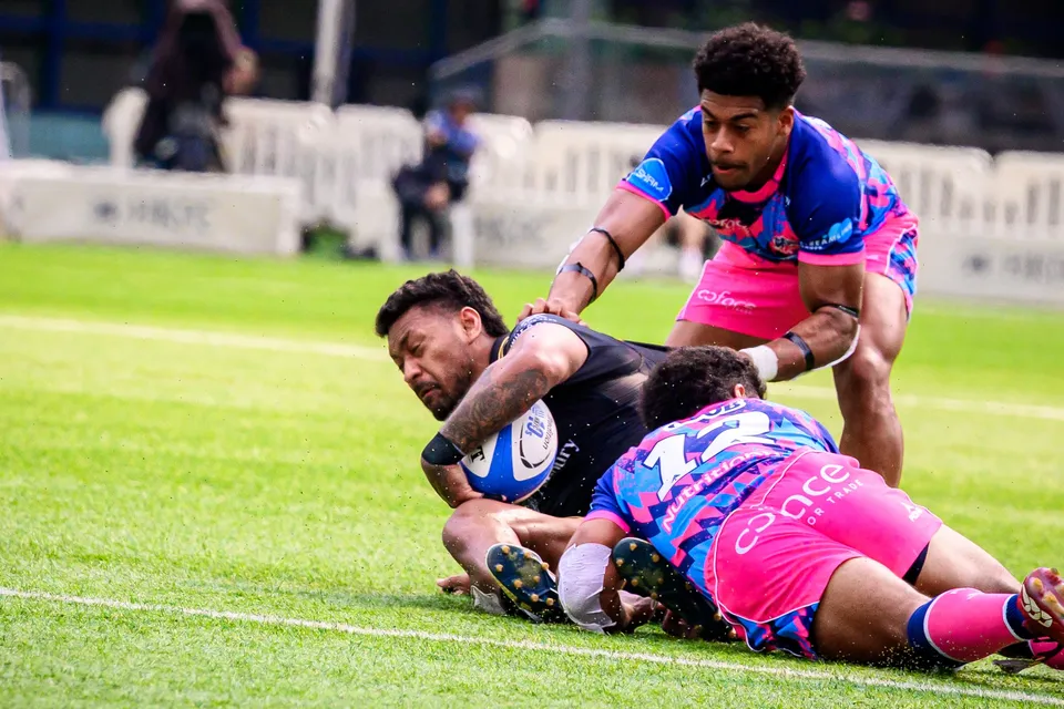 Tropics player in black lies on the ground clinging to the ball as OSOB players in pink stand over him