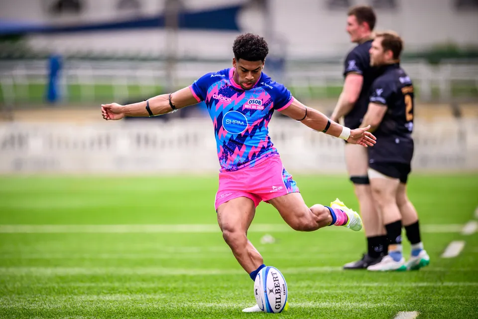 OSOB kicker in pink and blue strikes a place kick with Ashbury Tropics players in black waiting behind