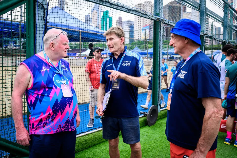 Three men talk beside a net fence, one in a pink and blue shirt and two in navy, 2026 HKFC 10s