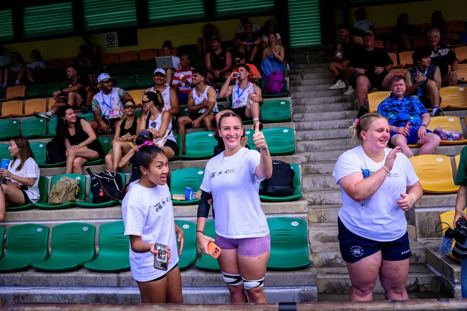 Three women in white team shirts stand in front of green and yellow seats, one giving a thumbs up, 2026 HKFC 10s