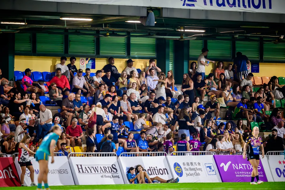 Packed stand of spectators above advertising boards, with players at the pitch edge, 2026 Tradition HKFC 10s
