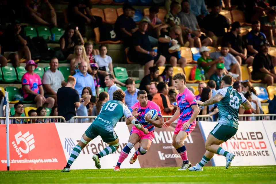 OSOB ball carrier in pink runs at the Froggies Club defence in front of a crowded stand and sponsor boards