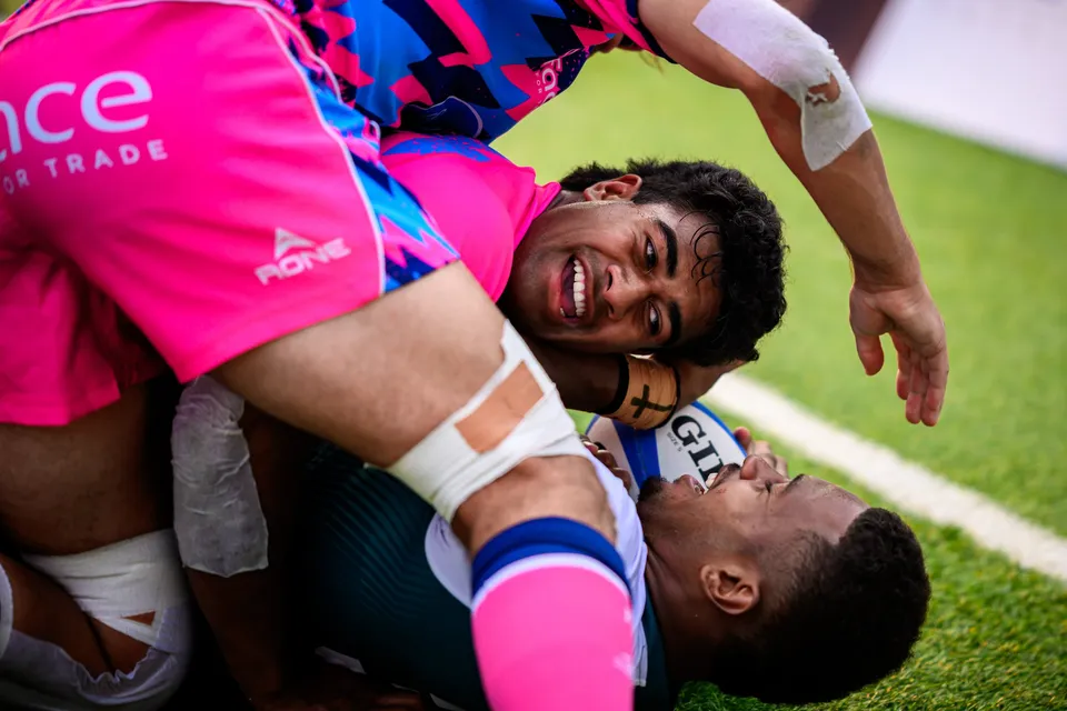 Close-up of a smiling OSOB player lying across a pile of tackled players, a Froggies Club player pinned beneath