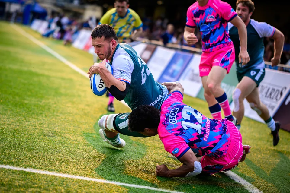 Froggies Club player in green dives forward with the ball as an OSOB defender in pink tackles low