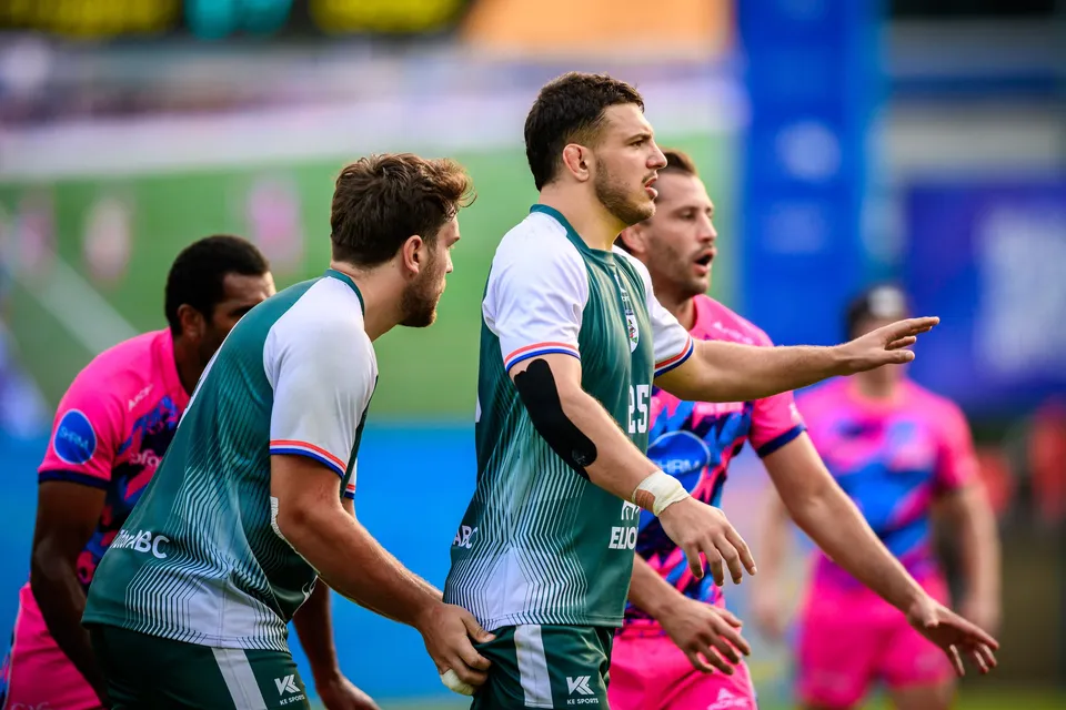 Two Froggies Club forwards in green stand in the foreground as OSOB players in pink gather behind them