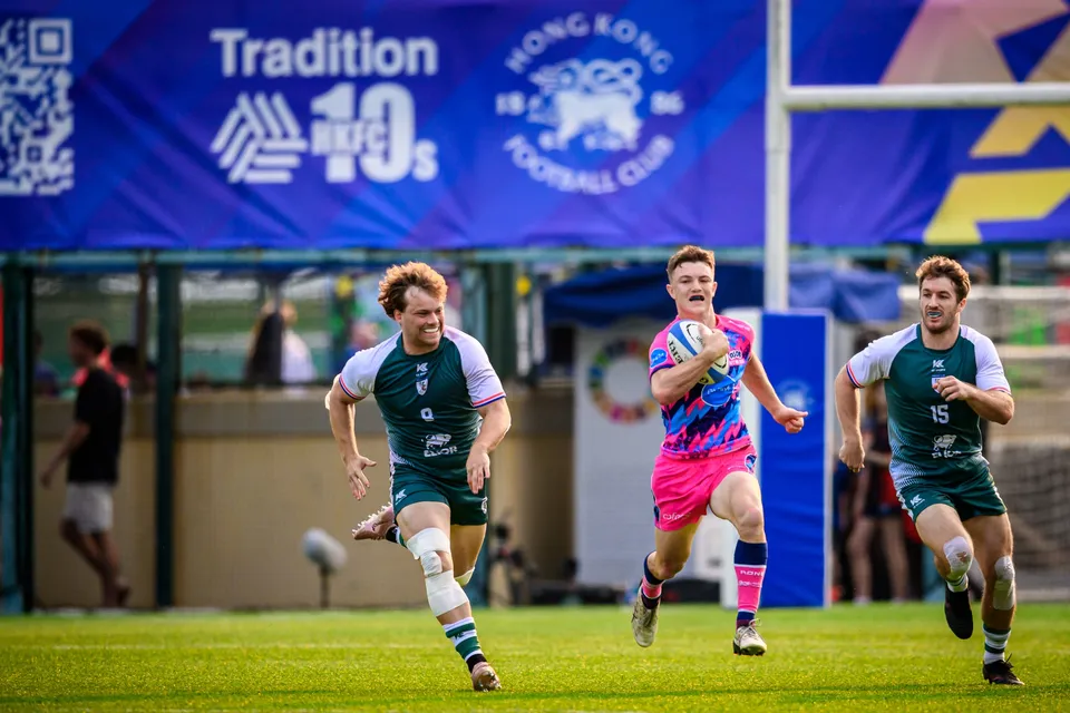 OSOB ball carrier sprints between two Froggies Club chasers beneath a Tradition HKFC 10s banner