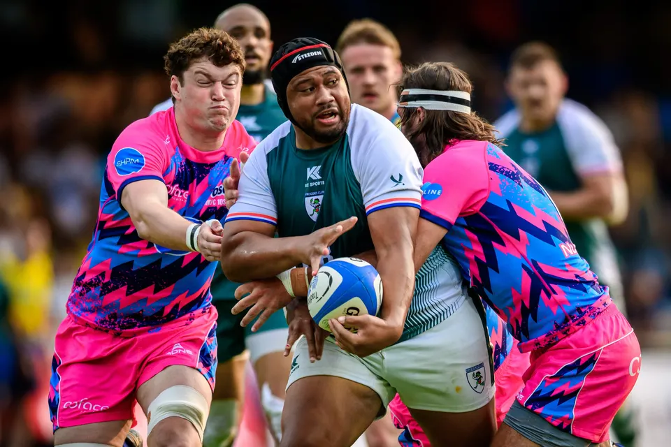 Froggies Club player in a scrum cap holds the ball in both hands as two OSOB players close in on him