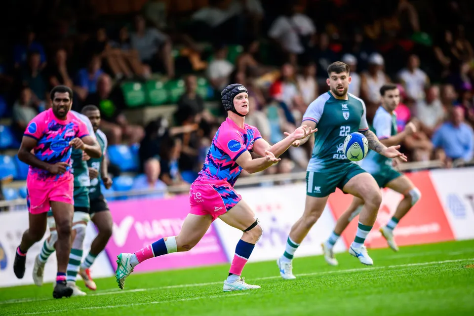 Froggies Club number 22 passes the ball while an OSOB player in a scrum cap and pink shorts runs across him