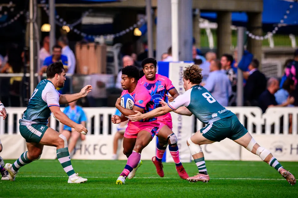 OSOB ball carrier is gripped by two Froggies Club defenders, one wearing number 8, with a trackside crowd behind