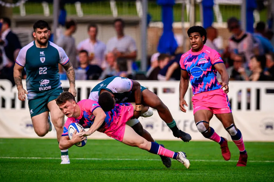 OSOB player falls forward with the ball as a Froggies Club tackler drags him down, another OSOB player looking on