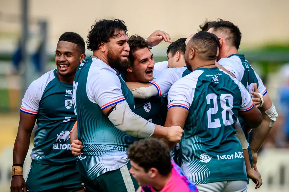 Froggies Club players in green grin and embrace in a celebratory huddle, an OSOB shirt visible at the bottom