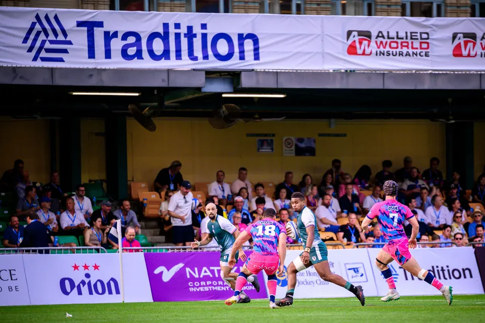 OSOB players in pink and blue chase a Froggies runner in green past the Tradition banner at the HKFC 10s