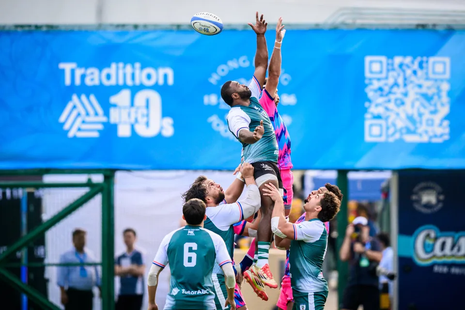 OSOB jumper reaches for a line-out ball above Froggies players in green and white, a blue HKFC 10s banner behind