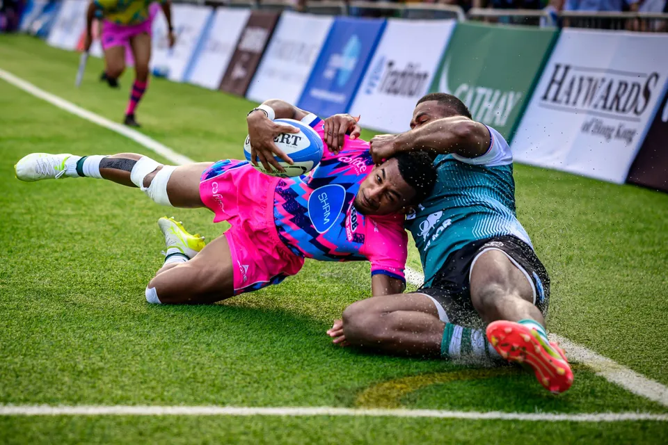 OSOB player dives sideways with the ball into touch beside advertising boards as a Froggies defender slides in