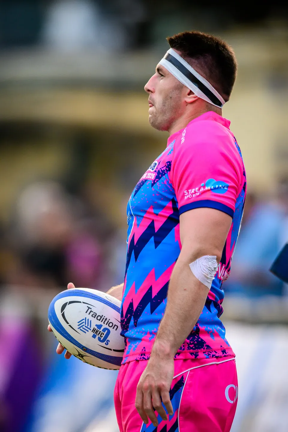 Side view of an OSOB player in a white headband standing still on the pitch holding a ball marked Tradition