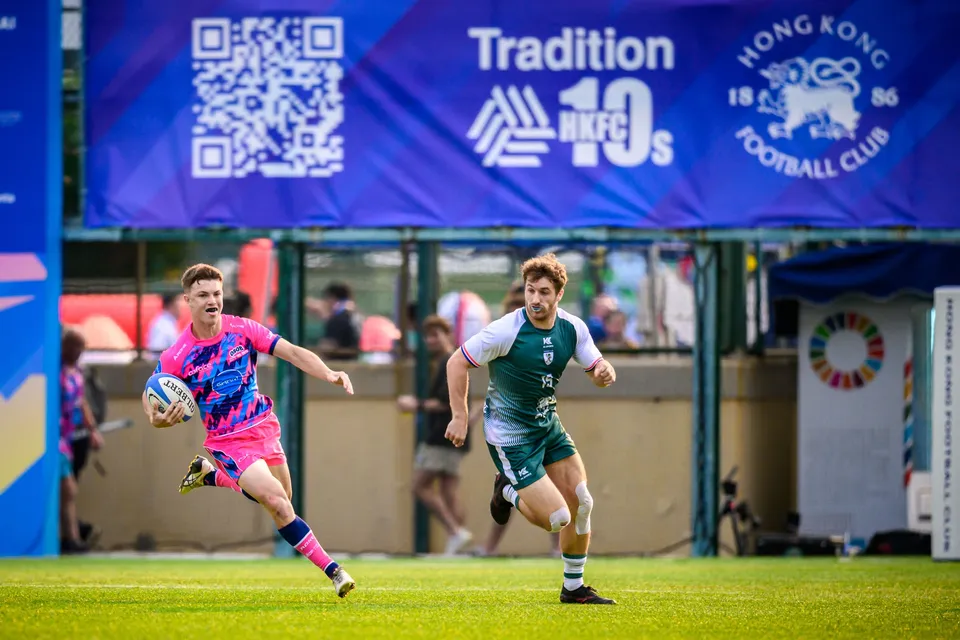 OSOB ball carrier sprints under the Hong Kong Football Club banner with a Froggies player in green chasing him