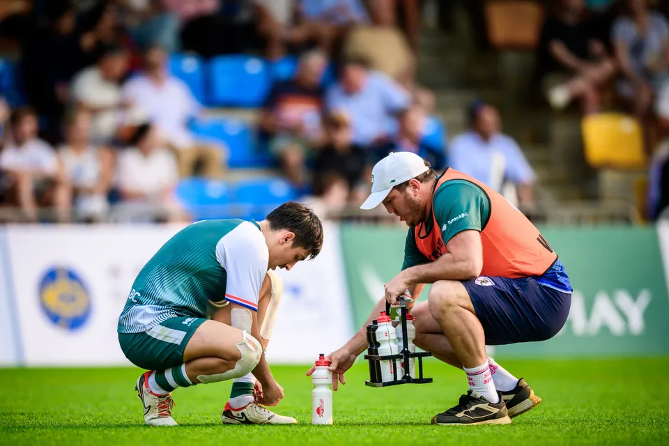 Froggies player in green and white crouches on the pitch as a man in an orange vest tends to his knee