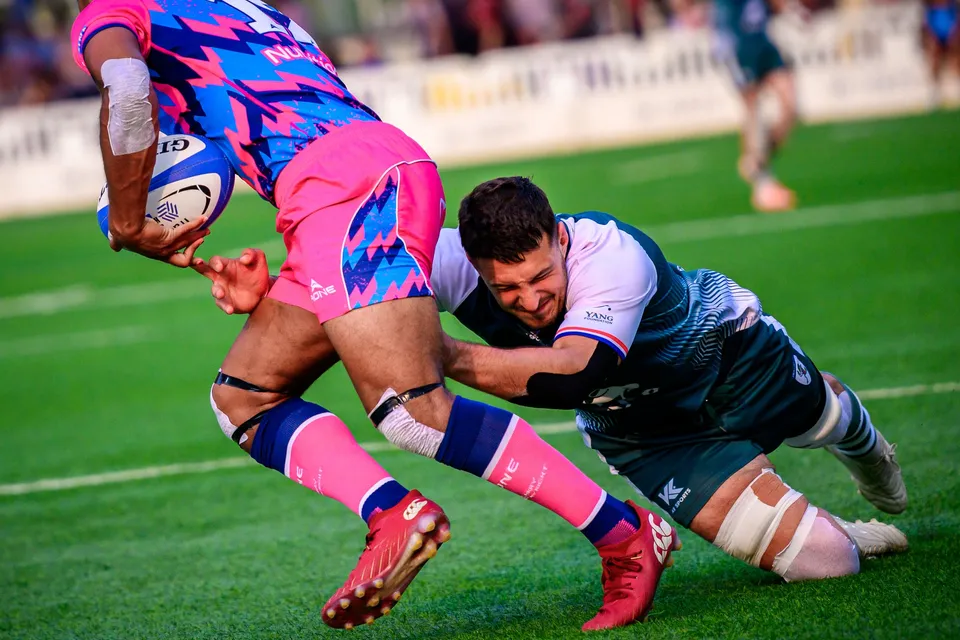 OSOB ball carrier in pink is grabbed round the waist by a Froggies defender in a low tackle on the grass