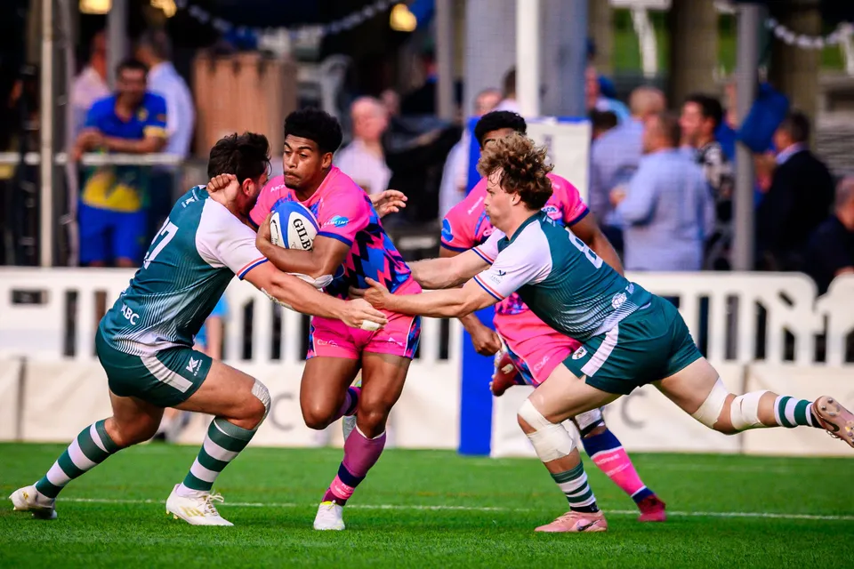 OSOB ball carrier is wrapped up by two Froggies Club defenders in green beside a trackside crowd