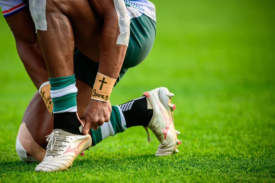 Close-up of a Froggies Club player in green socks bending to tie a white boot on the grass