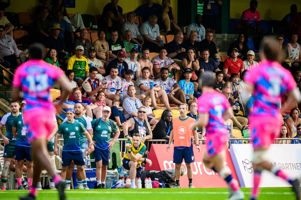 OSOB players in pink run past in the foreground as Froggies Club substitutes stand by the touchline