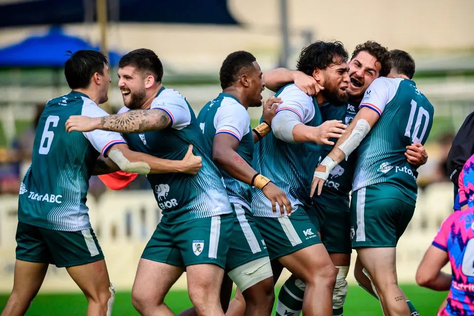 Froggies Club players in green hug and celebrate in a tight group, an OSOB shirt just visible at the edge
