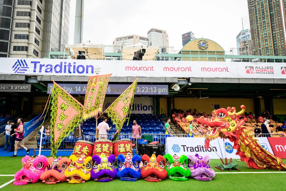 Row of colourful lion heads and a red dragon on the pitch below the Tradition boards, 2026 HKFC 10s opening