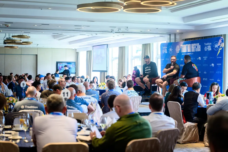 Wide view of a function room with chandeliers, round tables and a panel beside the sponsor backdrop, 2026 HKFC 10s