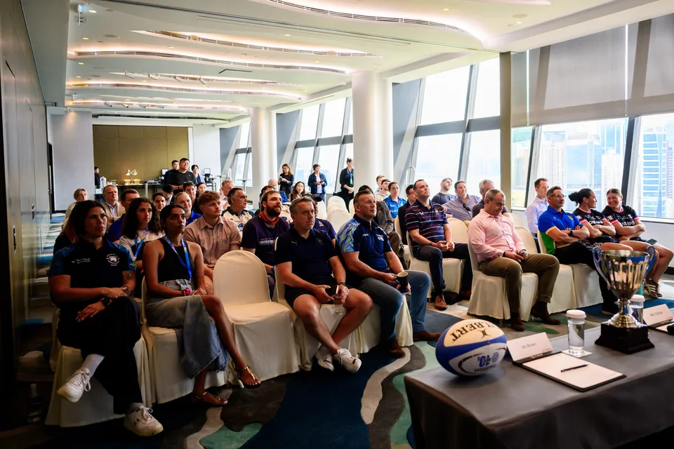 Audience on cream chairs listens to speakers, with a trophy and a rugby ball on a table, 2026 HKFC 10s