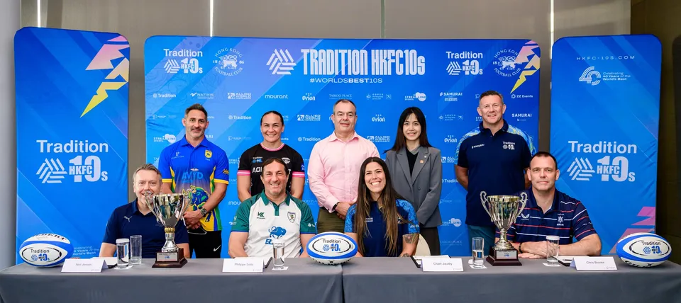 Panel and guests sit and stand behind a table of trophies and rugby balls at the 2026 HKFC 10s press conference