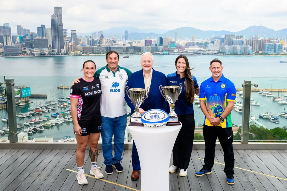 Five people pose with two trophies and a rugby ball on a harbourfront terrace, 2026 HKFC 10s press conference