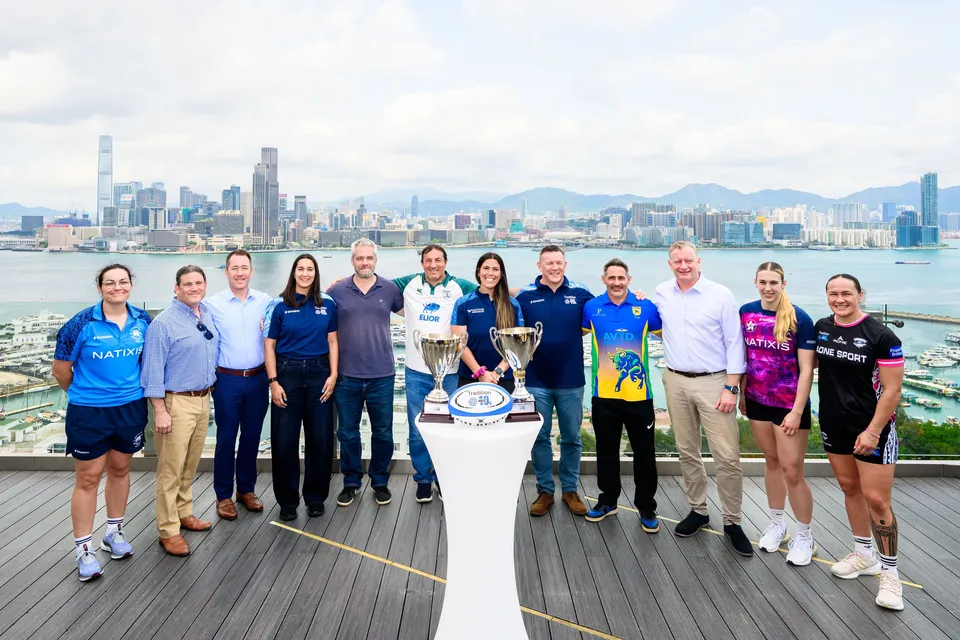 Twelve people in team and sponsor kit line up with two trophies on a terrace above the harbour, 2026 HKFC 10s