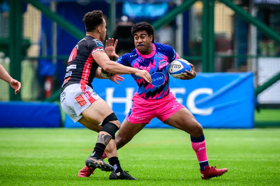 OSOB ball carrier tucks the ball under one arm as a black-shirted tackler grips him in front of blue HKFC boards