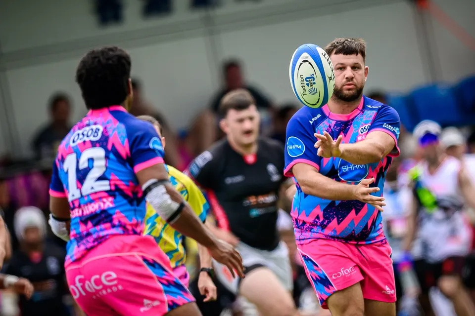Bearded OSOB player passes the ball as a team-mate in number 12 runs past in the foreground