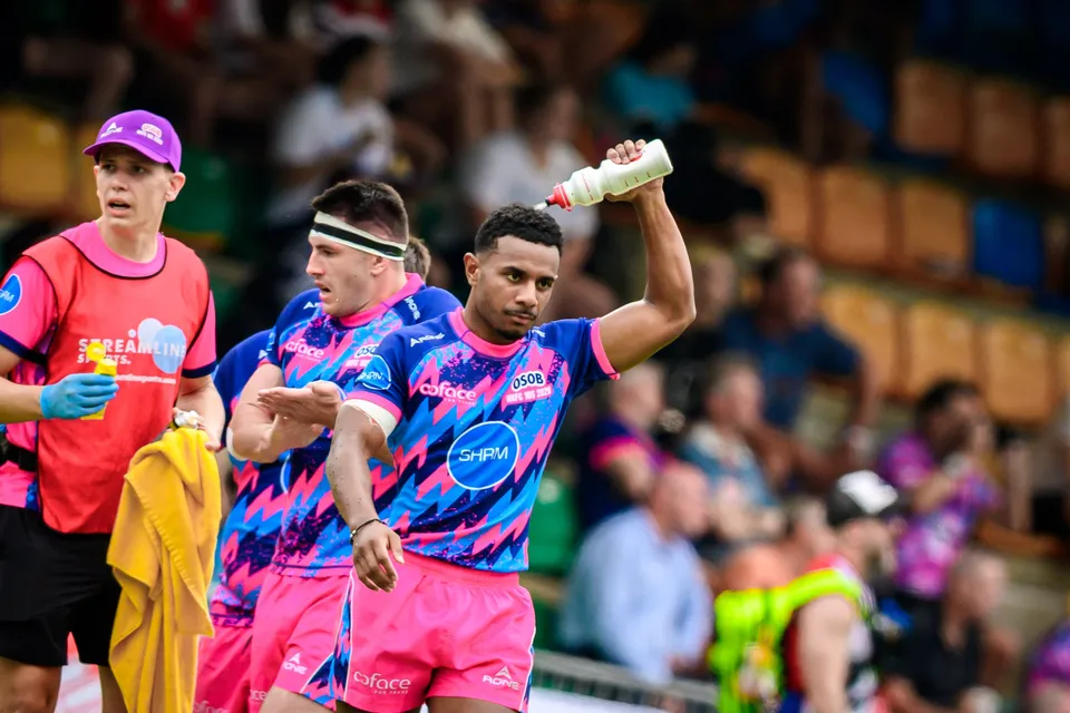 OSOB player raises a water bottle overhead during a break while a team-mate in a headband and a staff member look on