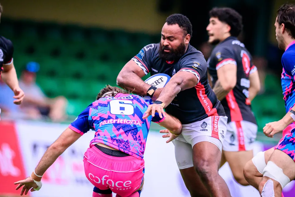 Large black-shirted ball carrier barrels into an OSOB number 6 defender as team-mates in black and pink run in support