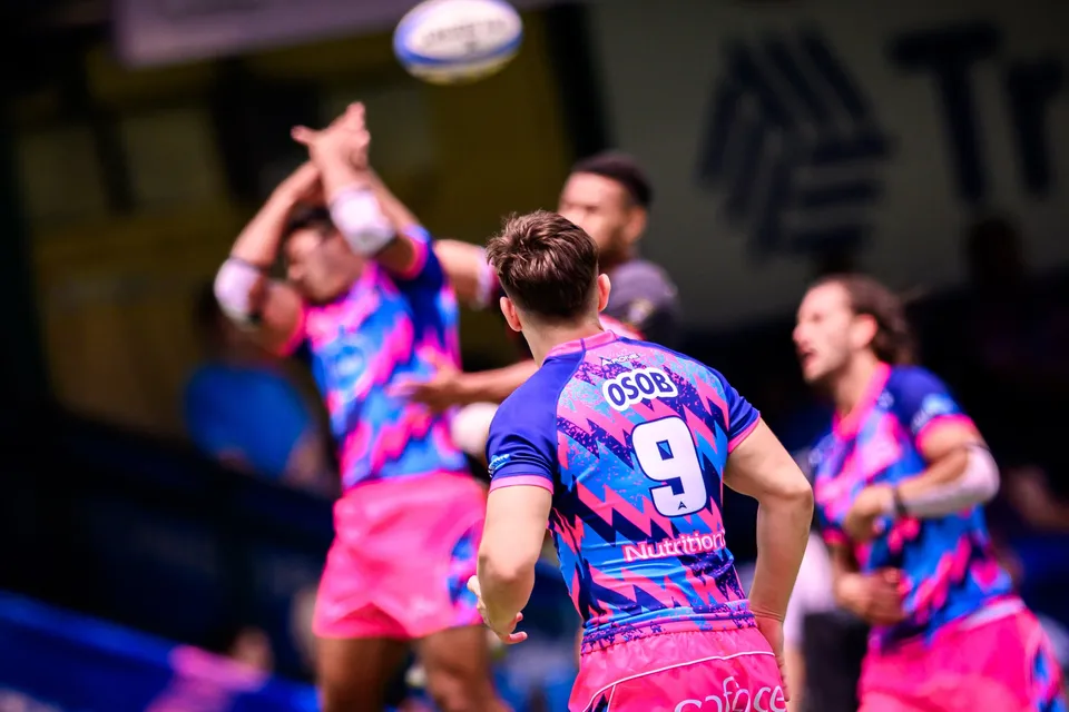 OSOB number 9 seen from behind as a blurred team-mate reaches up with both arms for a high ball