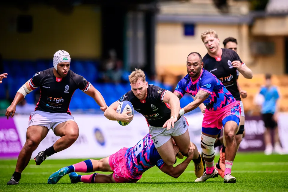 Black-shirted ball carrier runs through a tackle attempt from an OSOB player on the ground as team-mates run in support