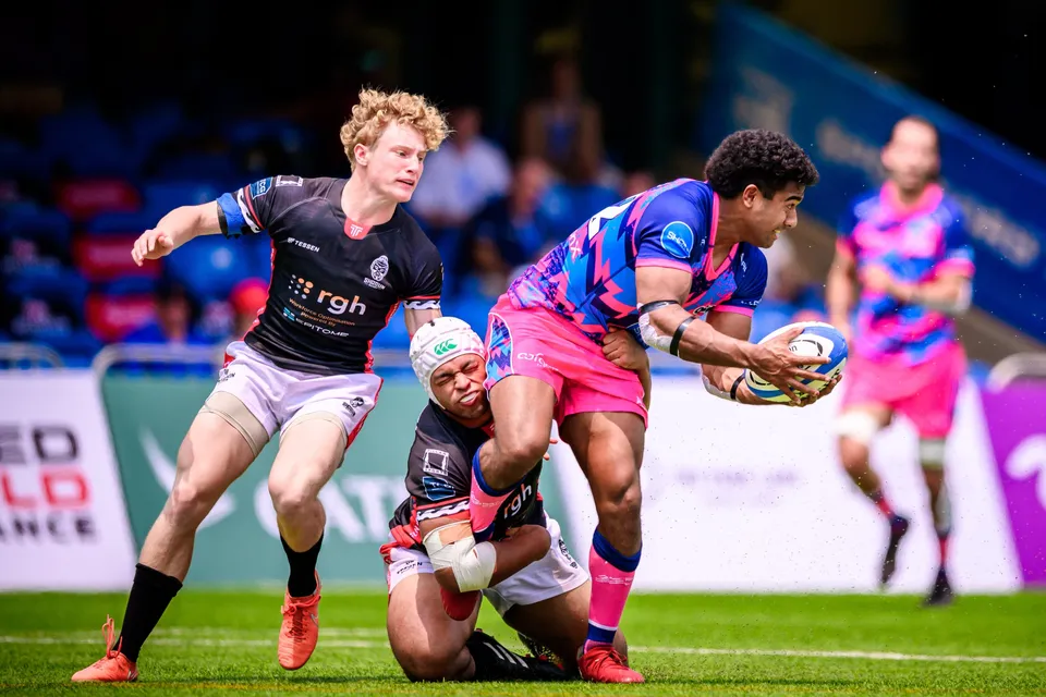 OSOB player offloads the ball as an RGH Shogun defender on his knees tackles him, a blond teammate in black beside them