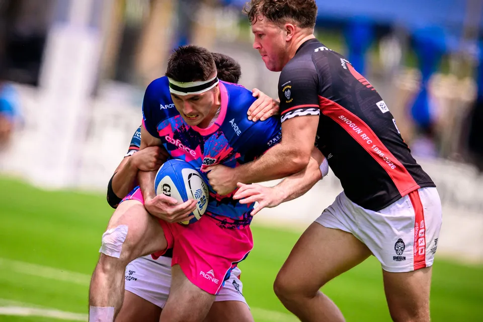 Close-up of a headbanded OSOB player clutching the ball as two RGH Shogun defenders in black and red wrap him up