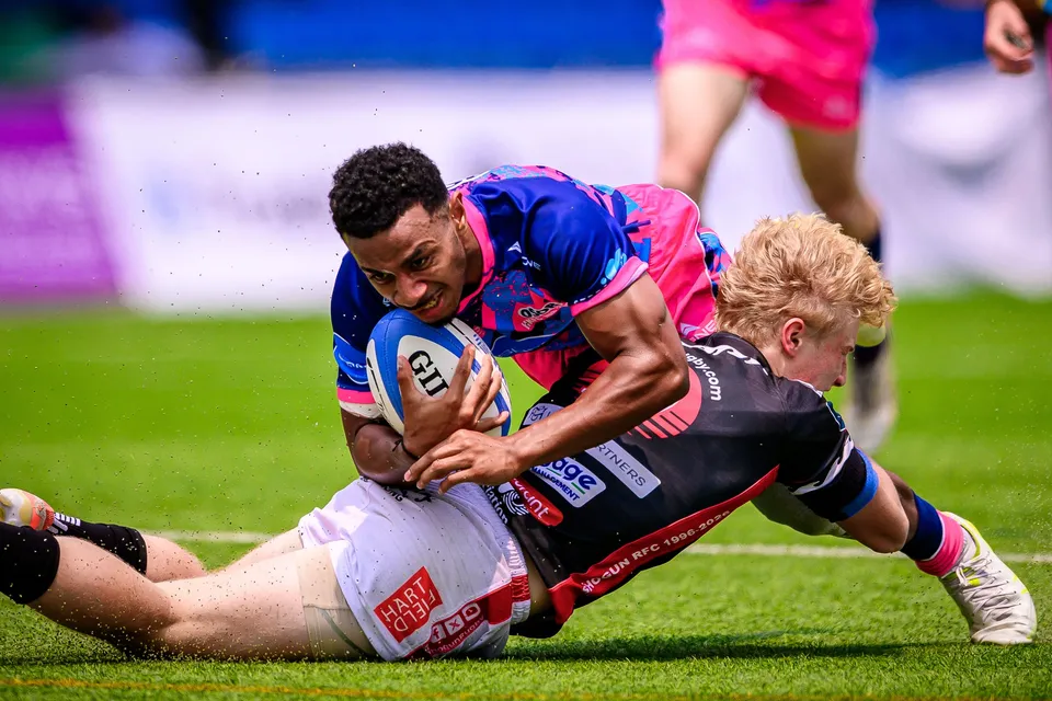 OSOB player stretches the ball out as a blond RGH Shogun defender in black drags him down onto the grass