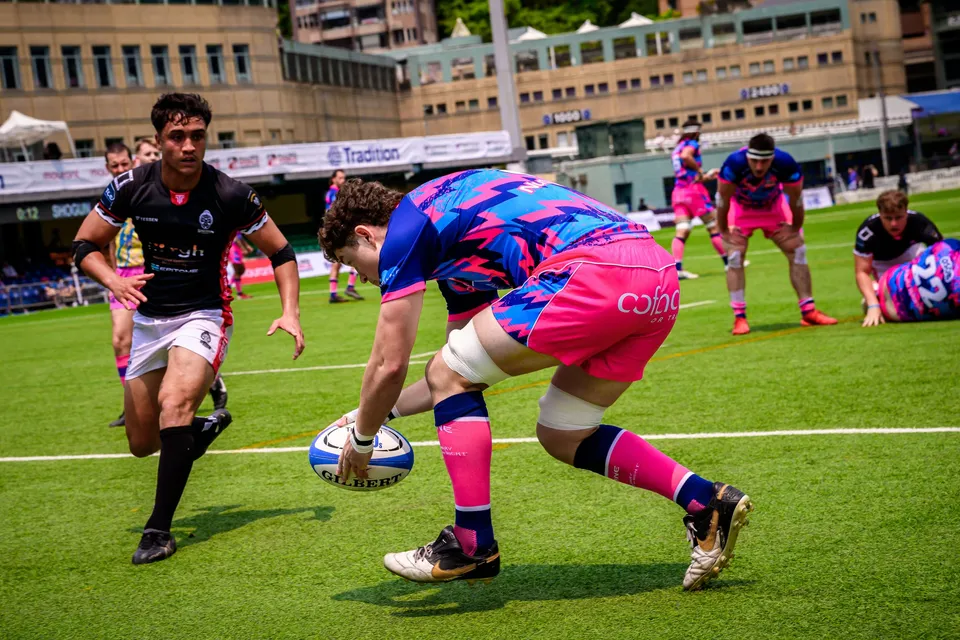 OSOB player in pink shorts bends low to ground the ball near the line while a black-shirted opponent looks on
