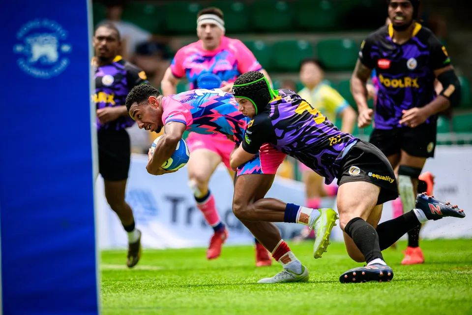 OSOB player dives for the line with the ball as a purple-kit defender grabs him, beside a blue padded post