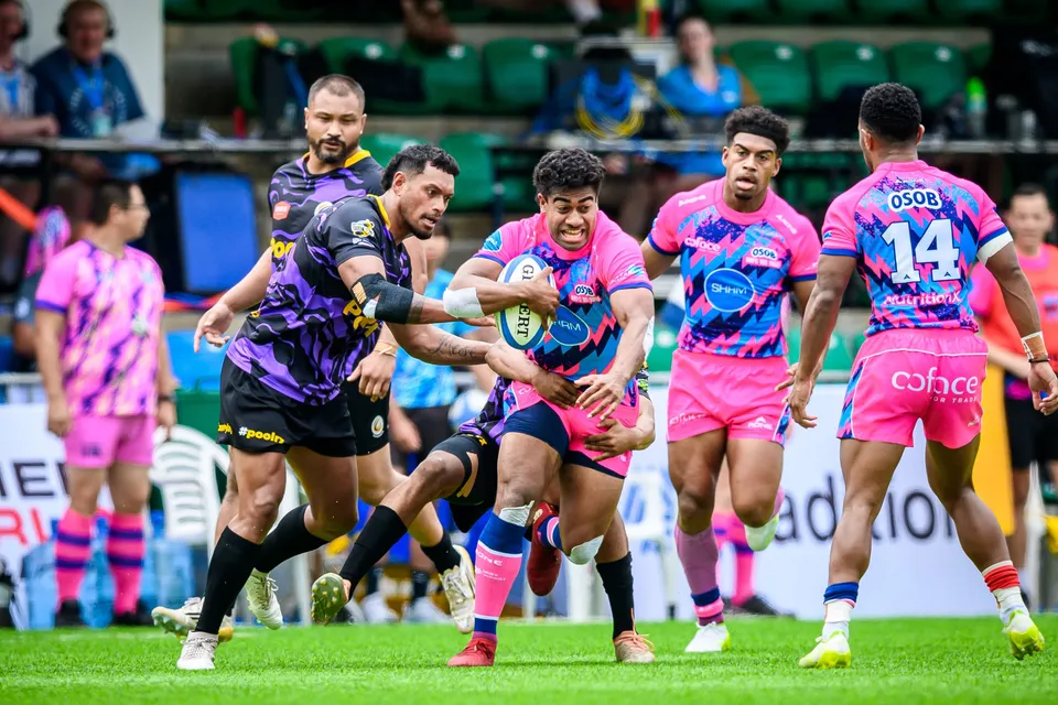 OSOB ball carrier is gripped by a purple-kit defender as pink-shirted number 14 and another team-mate run in support