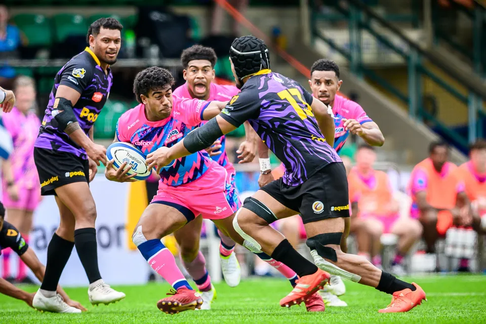 OSOB ball carrier twists in the grip of a headgear-wearing purple defender, with a pink team-mate behind